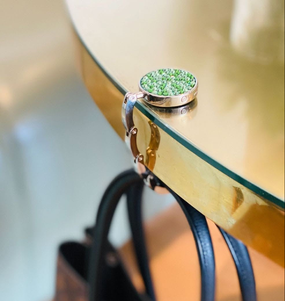 A Luxe Link hook resting on a white table edge with a bag hanging from its arm