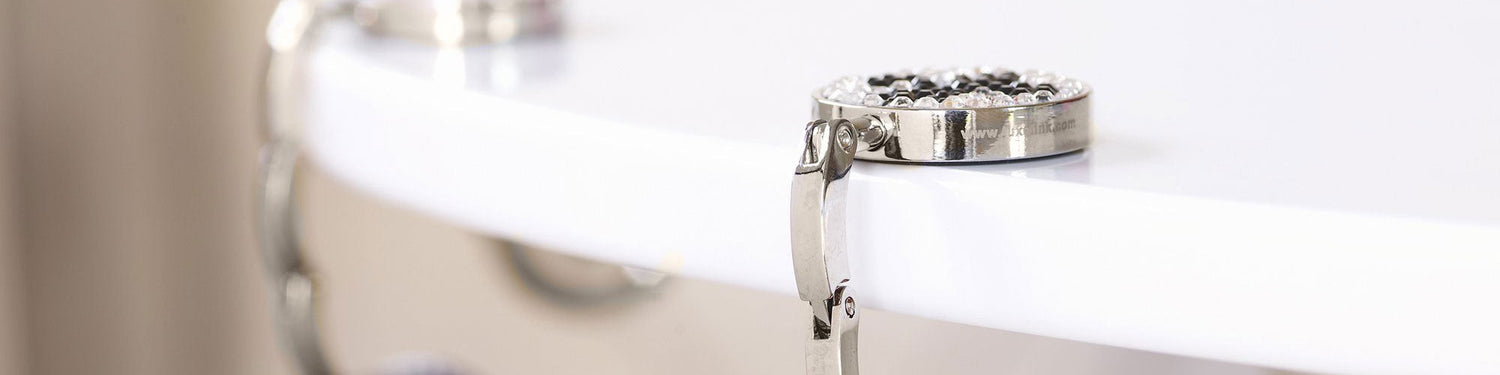 A Luxe Link hook with clear crystals clipped to the handle of a tan leather bag
