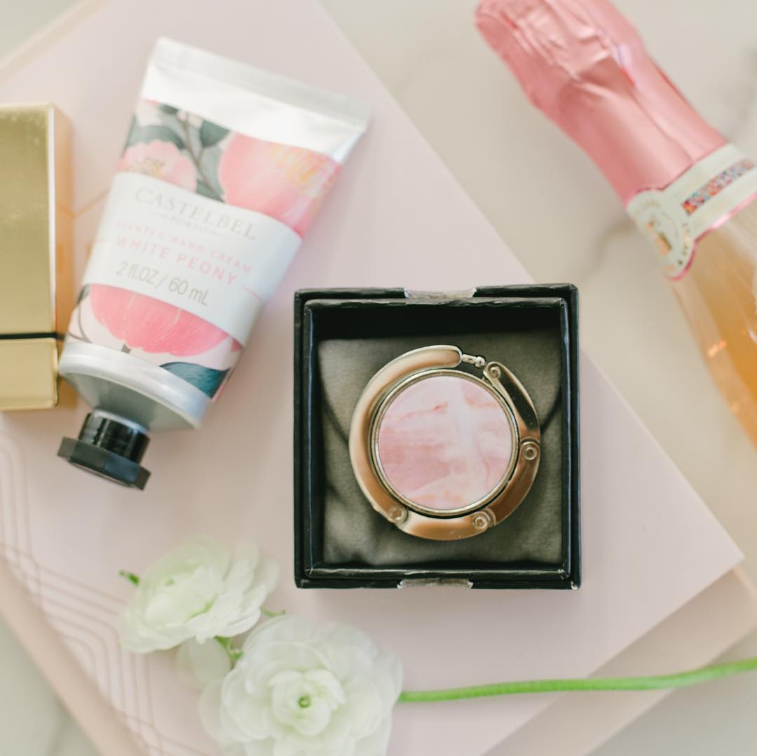Isabel purse hook in its black gift box beside hand cream and ranunculus