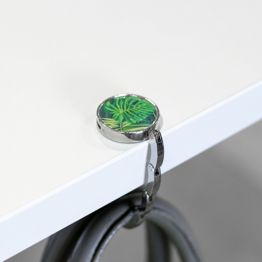 A Luxe Link hook resting on a white table edge with a bag hanging from its arm