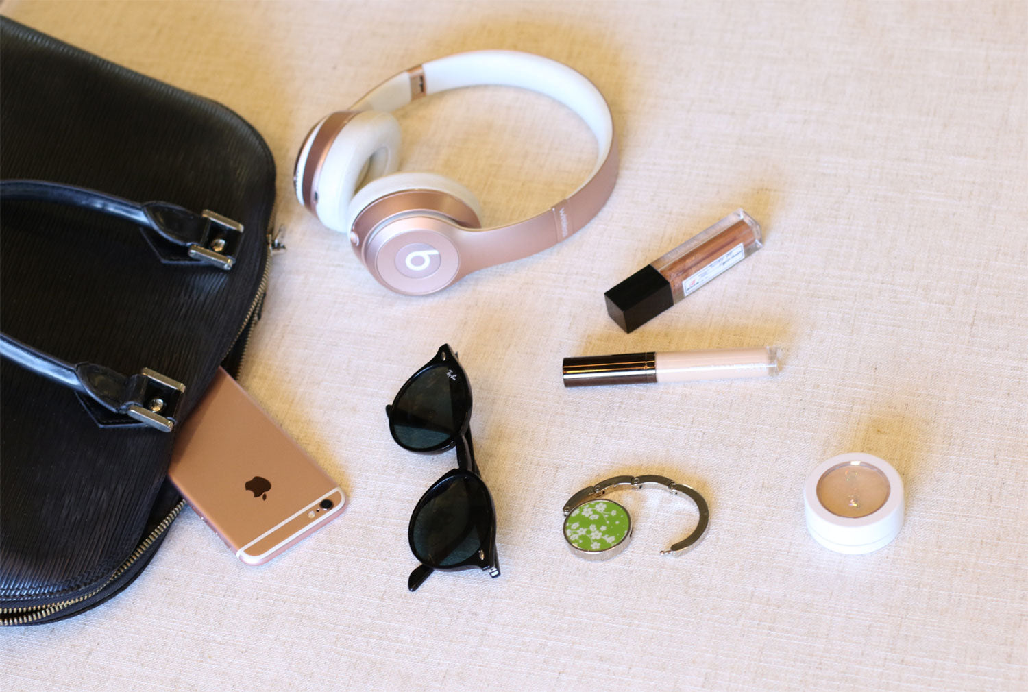 A bag, headphones, sunglasses and a green Luxe Link hook laid out on linen